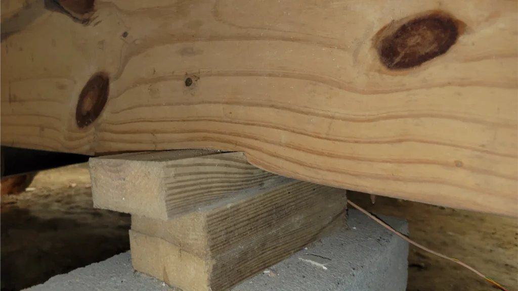A stack of wooden planks supports a wooden beam as a part of a foundation or structural support.